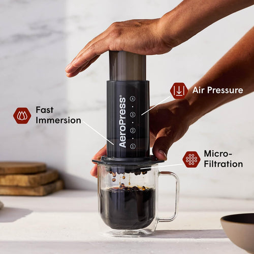 Hand pressing the AeroPress Original coffee maker into a glass mug, showing fast immersion and air pressure brewing