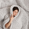 Woman sleeping peacefully wrapped in a light grey Bearaby Napper chunky hand-knit cotton weighted blanket