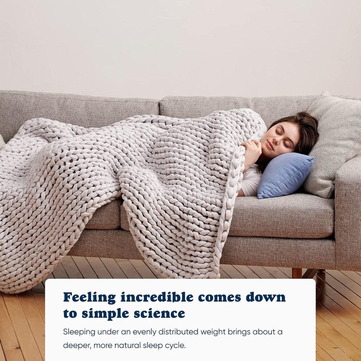 Woman napping on a grey couch under a light grey Bearaby Napper cotton weighted blanket, showing how evenly distributed weight supports deeper, more natural sleep