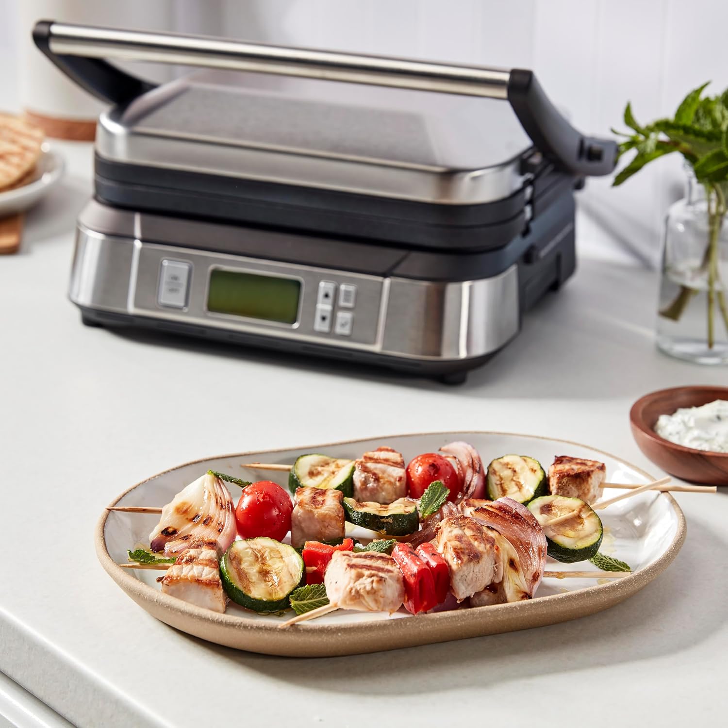 Cuisinart Griddler closed on a counter next to a plate of grilled chicken and vegetable skewers
