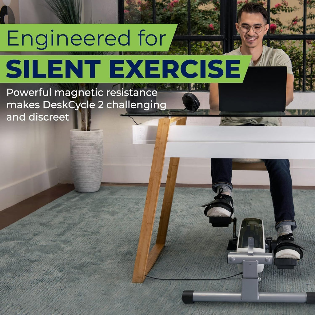 Man working at a standing desk while pedaling a DeskCycle 2 under-desk bike, text reads Engineered for silent exercise