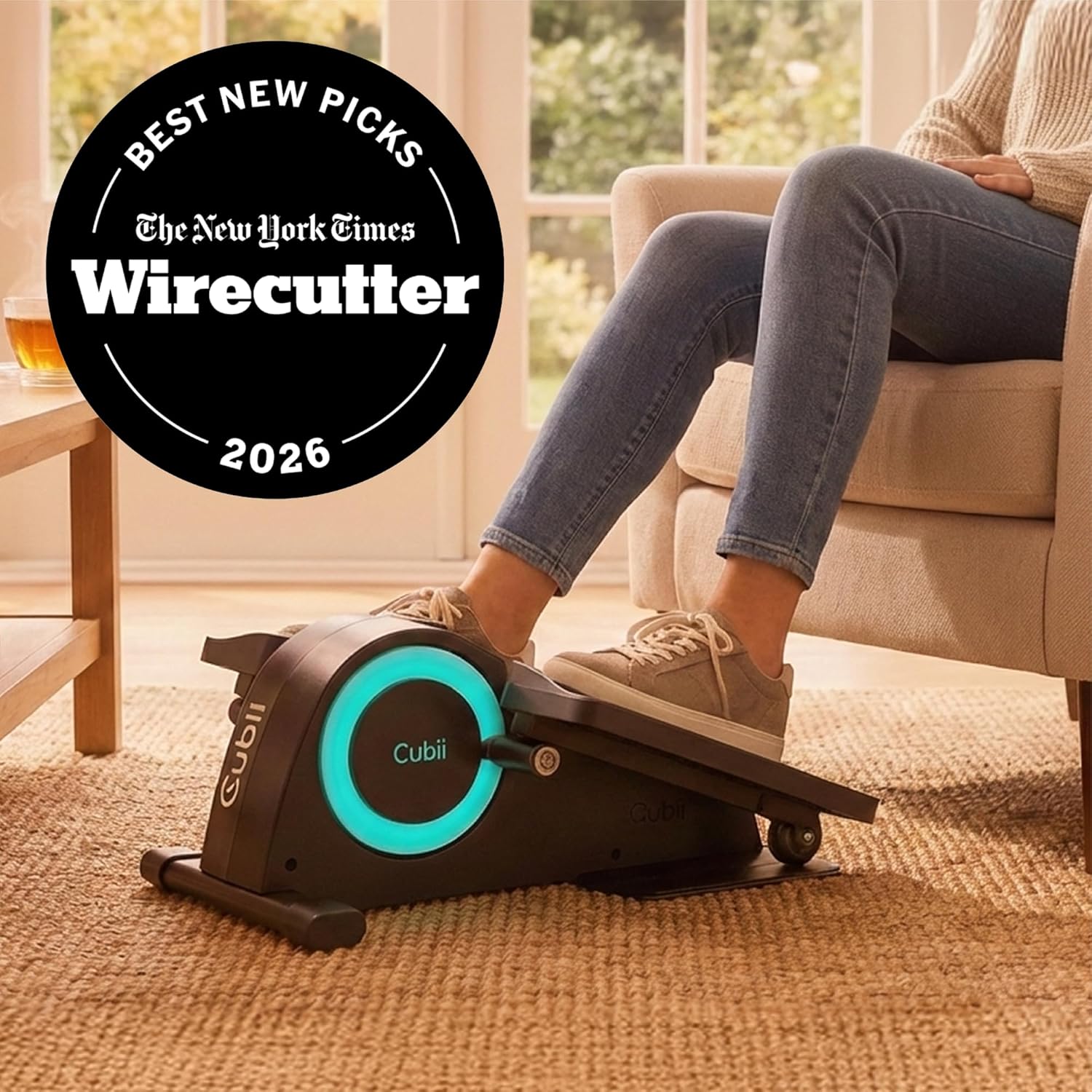Woman using the Cubii JR1 elliptical while seated in a living room armchair, with a New York Times Wirecutter Best New Picks 2026 badge