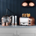 Dualit Classic 4-Slice Toaster in copper, shown on a kitchen counter with a matching kettle and cookware