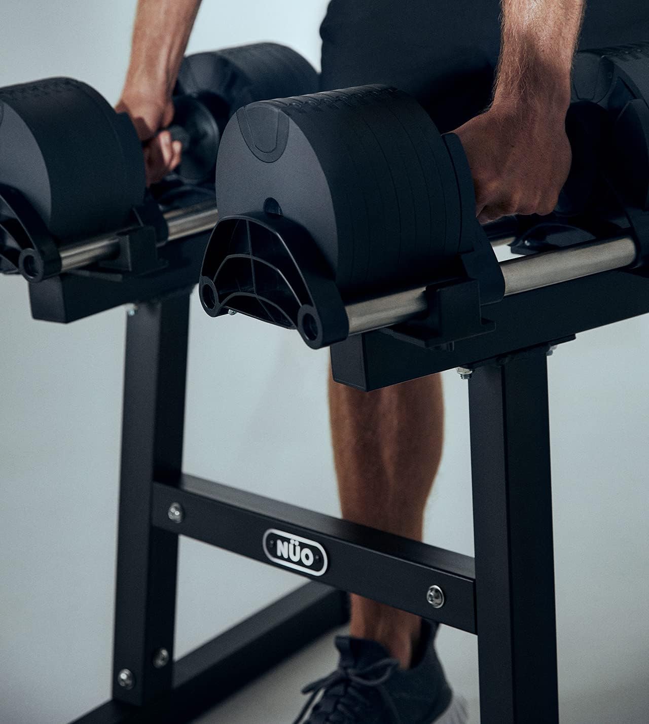 Close-up of hands lifting a NUOBELL adjustable dumbbell off its storage stand