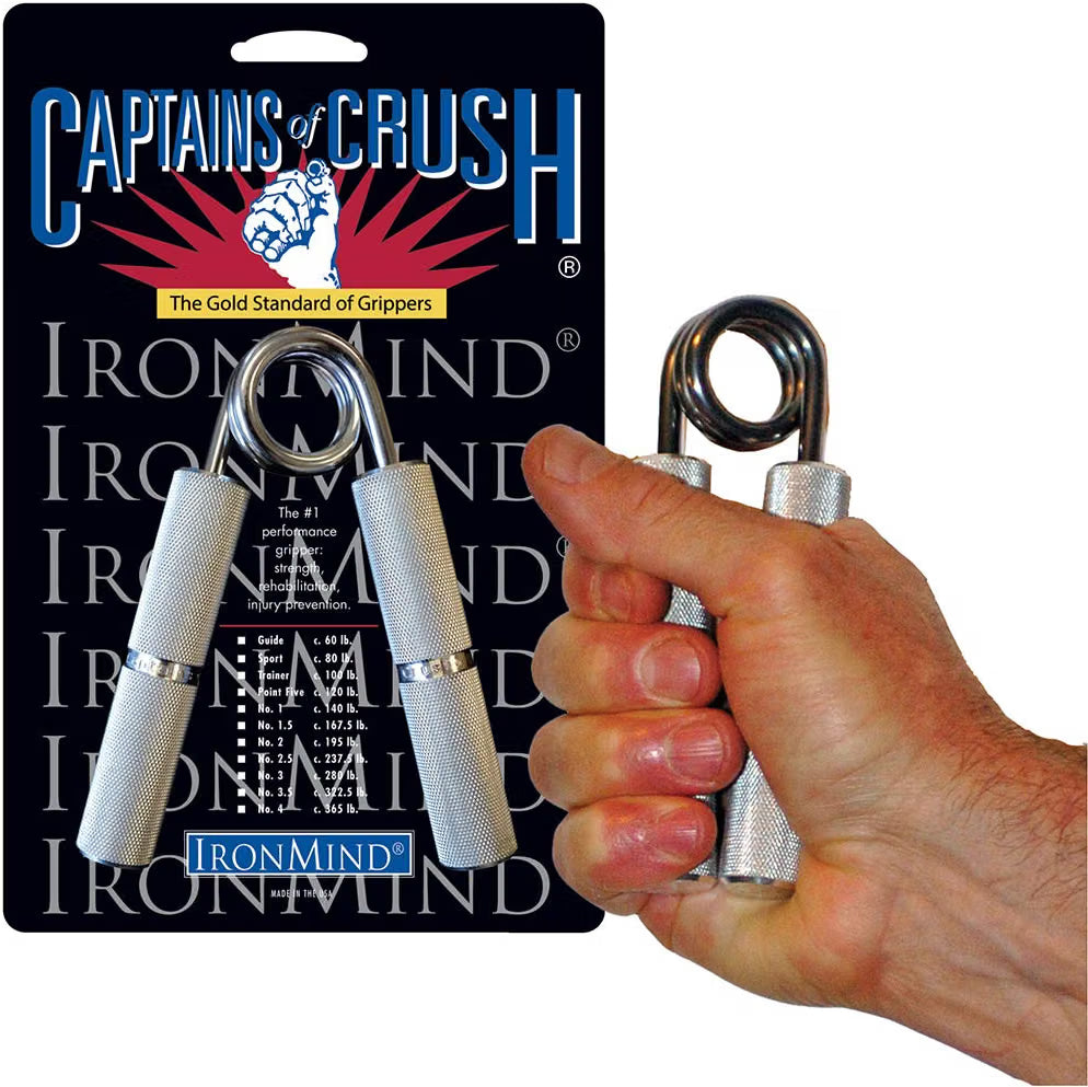 Hand squeezing an IronMind Captains of Crush hand gripper, shown with the product packaging