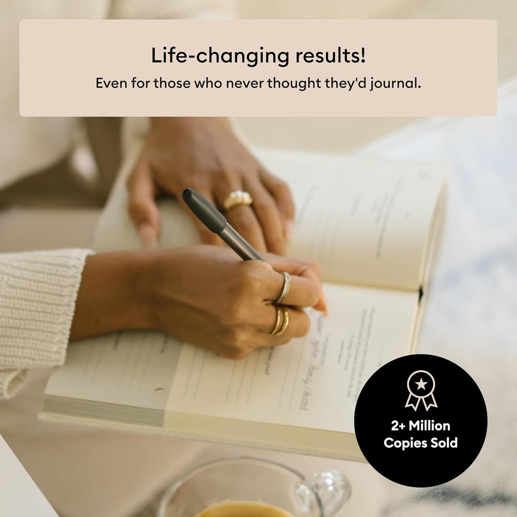 Hand writing in The Five Minute Journal with a cup of coffee nearby, noting over 2 million copies sold