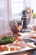 KitchenAid Artisan 5-Qt Stand Mixer in silver on a kitchen counter with baked bread nearby