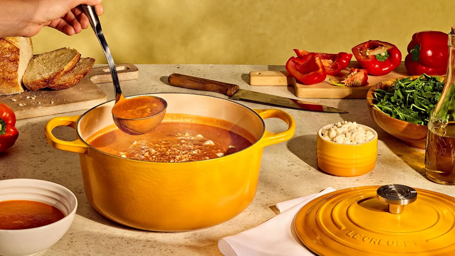 Le Creuset Signature Round Dutch Oven in a mustard yellow finish, filled with food as part of a table spread