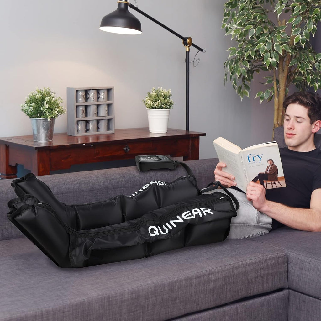 Man relaxing on a couch reading while using QUINEAR leg recovery compression boots for post-workout muscle recovery