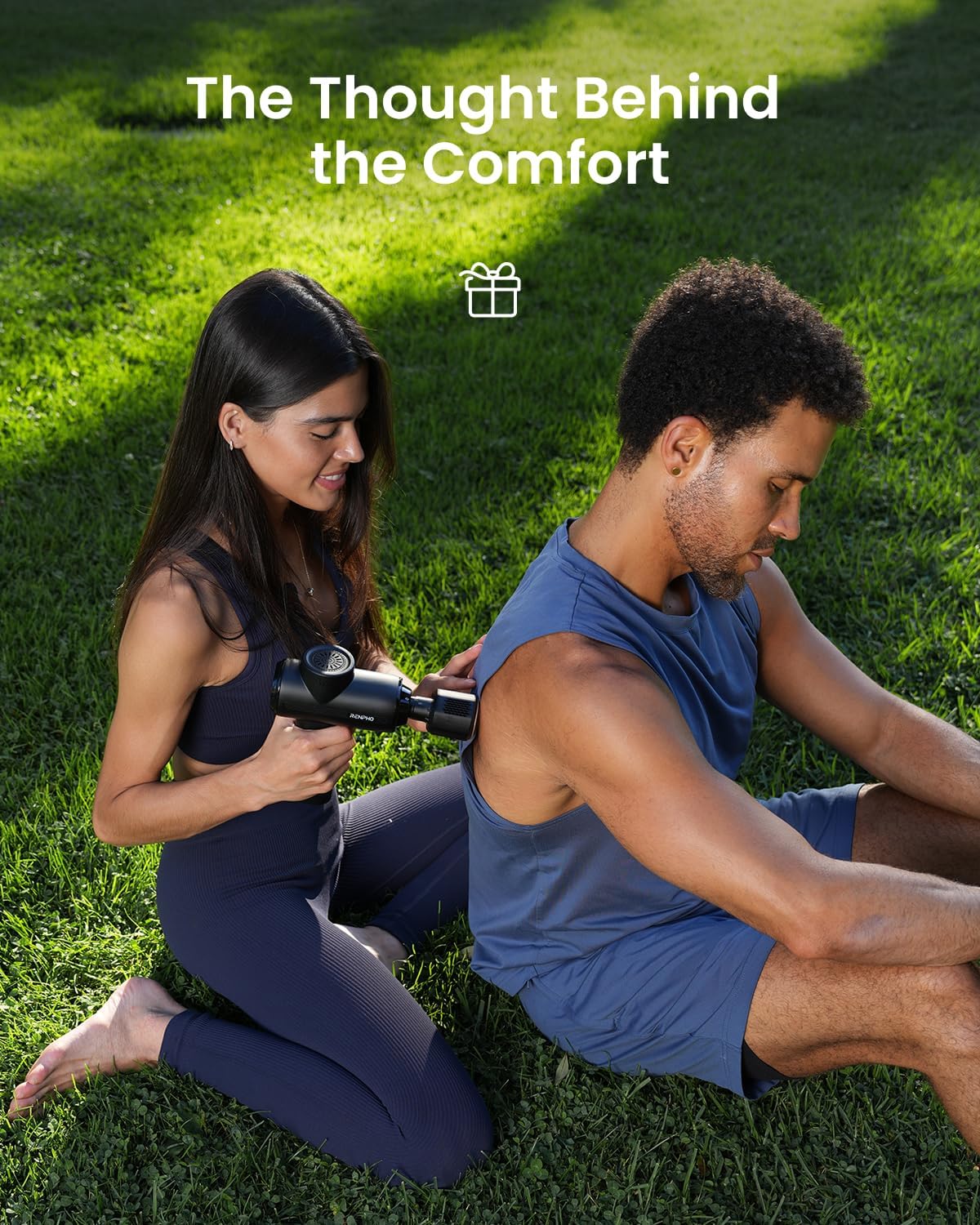 Woman using a RENPHO Active Thermacool 2 massage gun on a man's shoulder while sitting on the grass outdoors