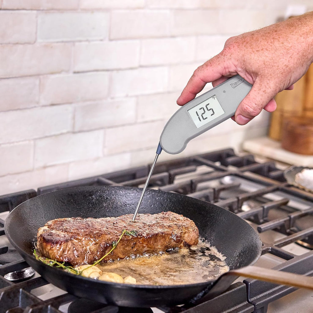 Hand holding a ThermoWorks Thermapen ONE to check a steak on a grill