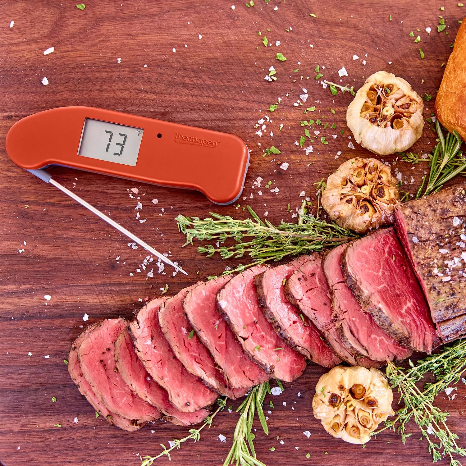 ThermoWorks Thermapen ONE in red, inserted into a sliced beef roast with rosemary and roasted garlic