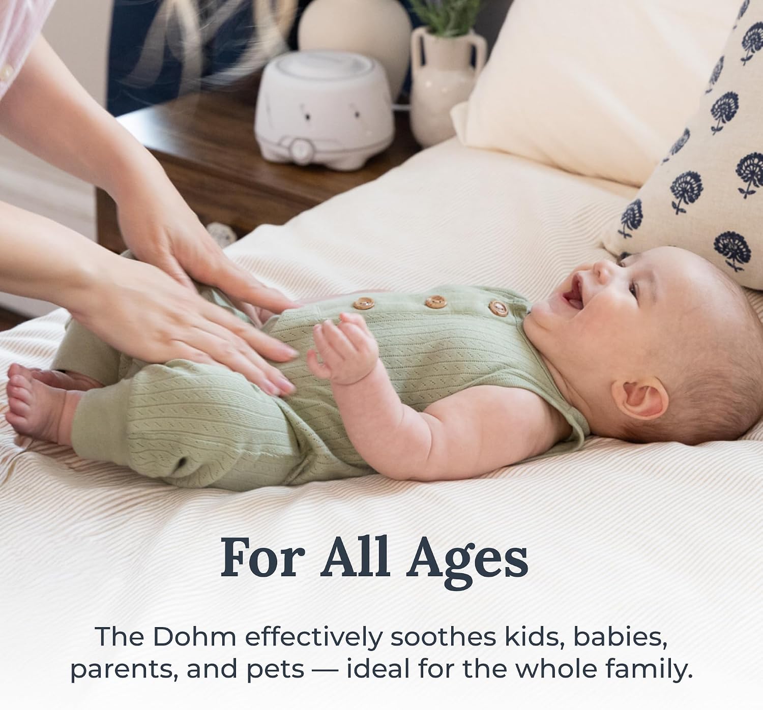 Hand adjusting the Yogasleep Dohm's control dial, graphic reading For All Ages
